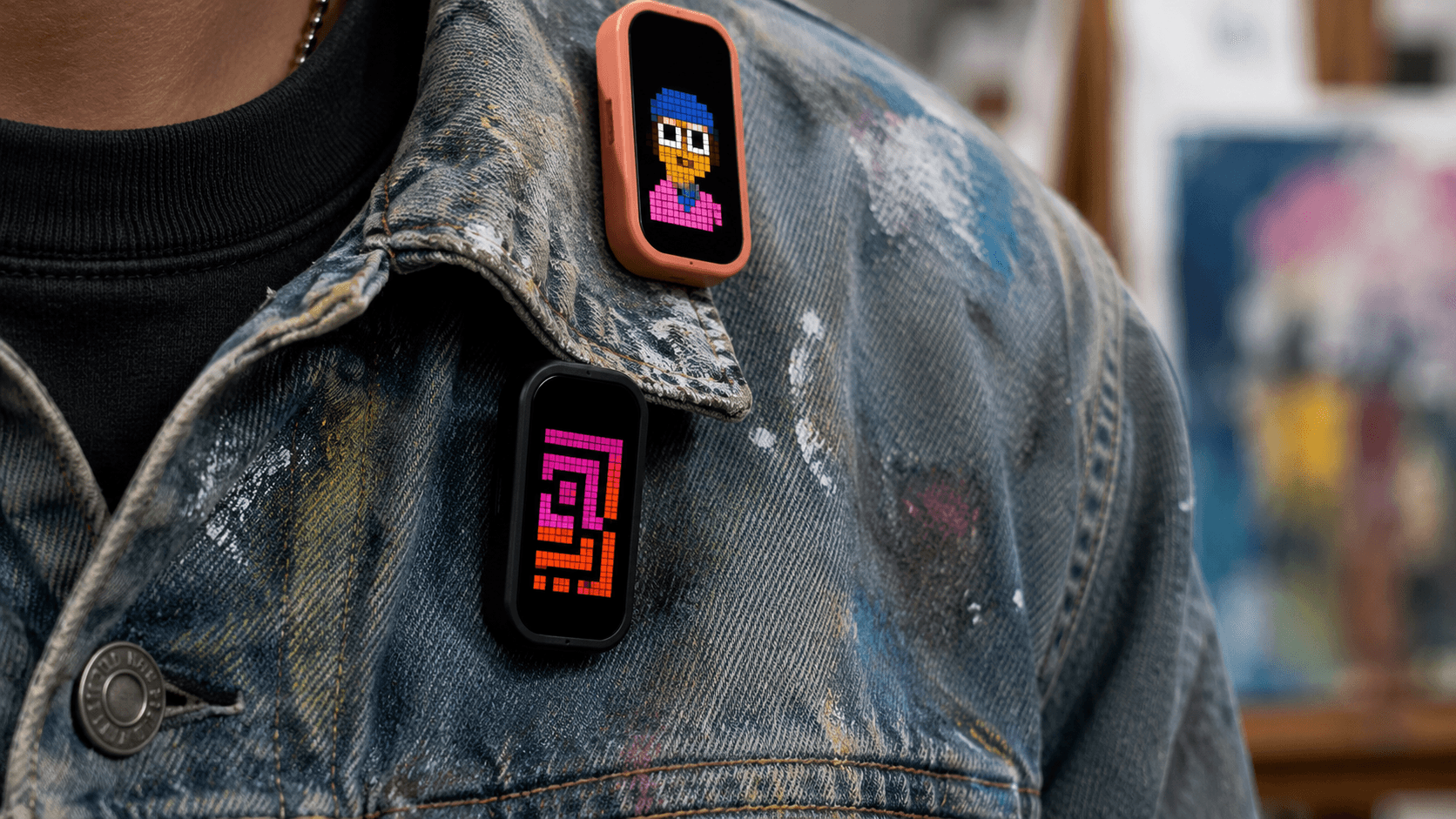 Two MoodPin units pinned to a paint-flecked denim jacket, each showing different pixel artwork