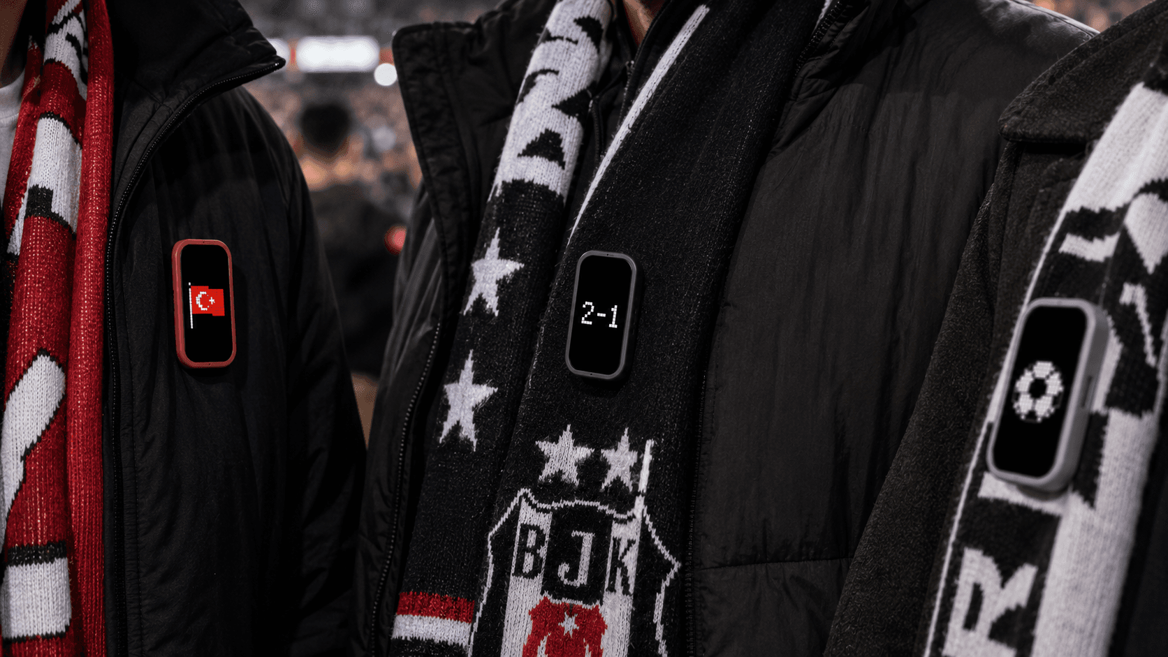 Supporters at a stadium wearing MoodPin units showing a flag, a match score and a crest